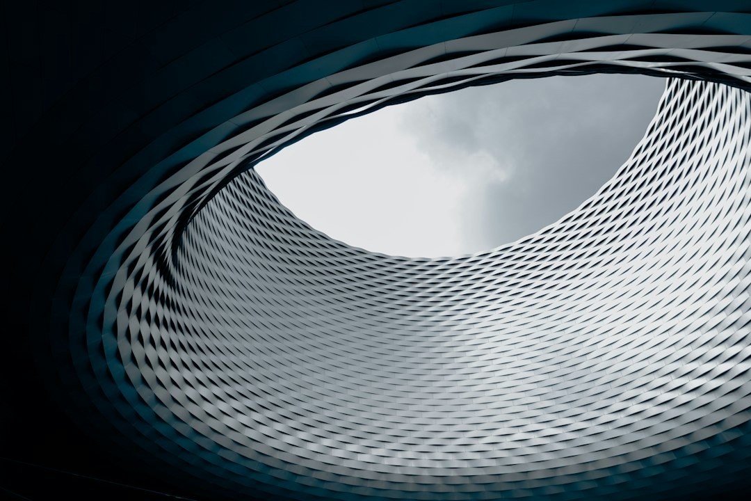 Curved metallic building structure with a round opening to clouds.